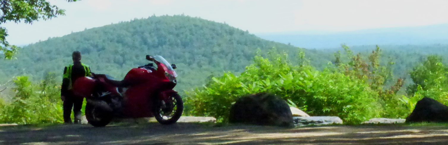 Red Honda VFR800 parked at a mountain overlook with the rider facing away from the camera, looking at the view