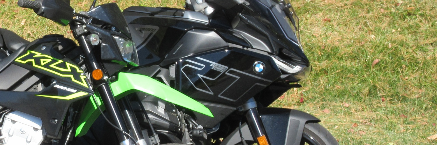small Kawasaki KLX300SM parked in front of a large, black BMW R 1300 RT touring motorcycle