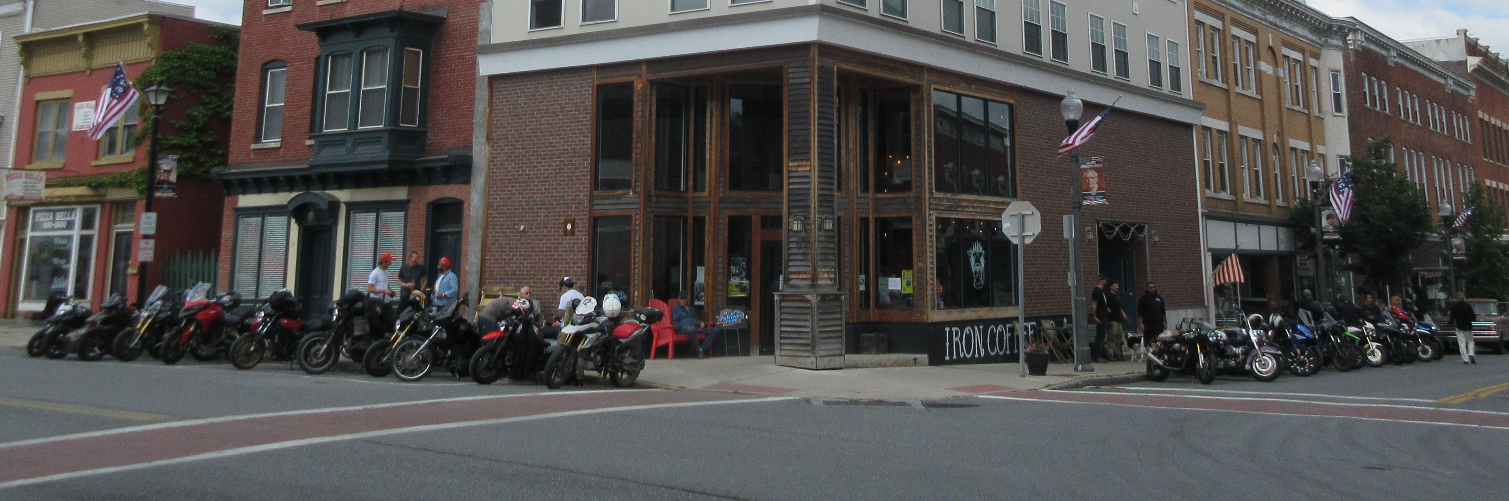 row of motorcycles parked in front of a small-town corner coffee shop