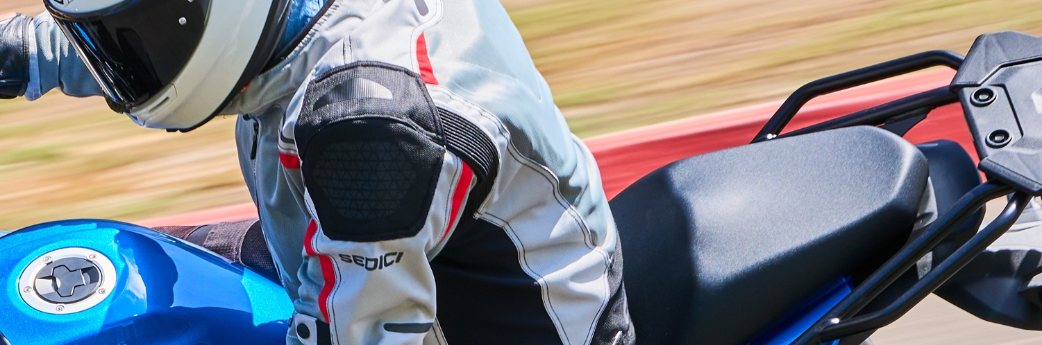 closely cropped view of the rider on a blue Suzuki wearing the silver Sedici Alexi 2 jacket with black and red accents